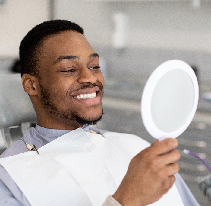 Man smiling while looking at reflection in handheld mirror