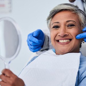 a patient smiling while checking her teeth with a mirror