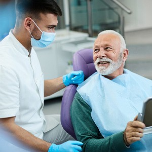 Senior patient looking at dentist while holding small mirror