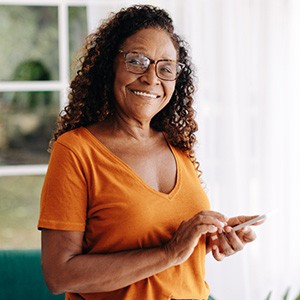 Senior woman with glasses smiling while looking at phone